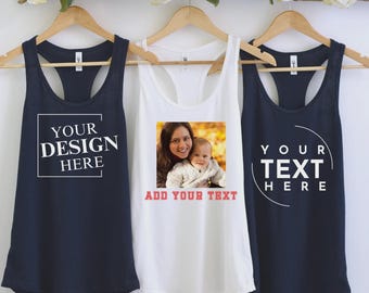 Könnte beinhalten: Drei Tanktops hängen an Holzbügeln. Ein marineblaues Tanktop hat den Text "YOUR DESIGN HERE" in einem weißen Feld. Das weiße Tanktop hat ein Foto und den Text "ADD YOUR TEXT". Das andere marineblaue Tanktop hat den Text "YOUR TEXT HERE".