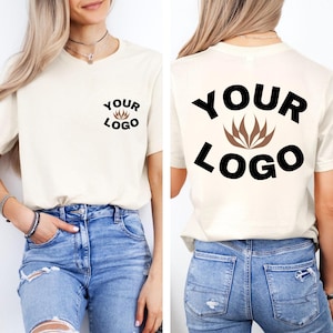 Puede incluir: Camiseta color crema con mangas cortas y cuello redondo. La parte delantera de la camiseta presenta un pequeño logotipo con el texto "YOUR LOGO". La parte trasera de la camiseta tiene una versión más grande del logotipo y el texto.