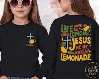 Könnte beinhalten: Schwarzes Sweatshirt mit Kreuz- und Zitronen-Grafik. Die Vorderseite zeigt ein kleines Kreuz- und Zitronen-Design mit dem Wort "Custom". Auf der Rückseite steht der Text "Life gave me some lemons but my Jesus he be makin' lemonade".
