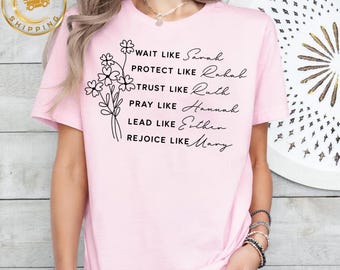 Könnte beinhalten: Hellrosa T-Shirt mit dem Text "WAIT LIKE Sarah, PROTECT LIKE Rahab, TRUST LIKE Ruth, PRAY LIKE Hannah, LEAD LIKE Esther, REJOICE LIKE Mary." Auf der linken Seite befindet sich ein Blumendesign. Das Wort "Pink" steht unten.