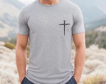 Könnte beinhalten: Hellgraues Rundhals-T-Shirt mit einem schwarzen Kreuzdesign auf der linken Brust. Das Kreuz besteht aus Nägeln. Das Shirt ist ein kurzärmliges, lässiges Oberteil.
