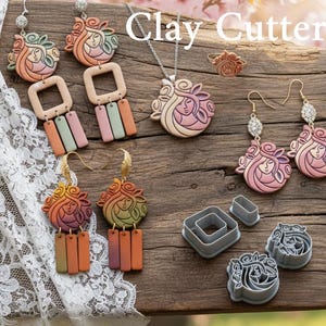 Puede incluir: Una colección de joyas de arcilla hechas a mano y cortadores de arcilla. Las joyas incluyen aretes, un collar y un anillo, todos con un diseño de rostro femenino en tonos de rosa, naranja y verde. Los cortadores de arcilla tienen formas cuadradas y florales.