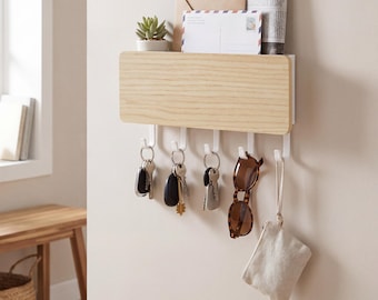 May include: A wall-mounted key and mail organizer made of light wood and white plastic. The organizer has a shelf for mail and a small plant, with hooks below for keys, sunglasses, and a small bag. The keys are attached to keychains.