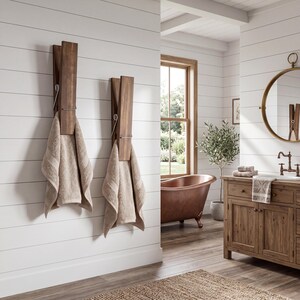 May include: Two wooden clothespin-style towel holders mounted on a white wall, each holding a beige towel. The holders have a dark brown finish and a silver metal hinge. The bathroom has a rustic, spa-like aesthetic.