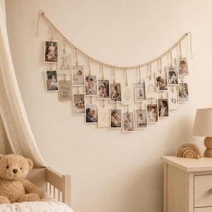 May include: A wall-mounted photo display garland featuring a long string of light-colored wooden beads. Numerous rectangular photo prints and illustrated cards are suspended from the beads by small wooden clips, creating a cascading arrangement.