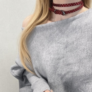 Puede incluir: Un collar gargantilla burdeos con lunares blancos y una hebilla plateada. La gargantilla de doble capa está hecha de un material suave y se lleva alrededor del cuello. El collar es un accesorio de moda.