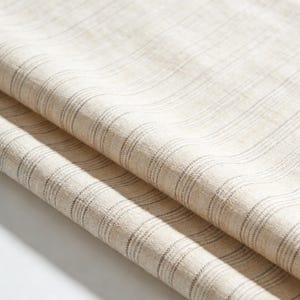 Puede incluir: Primer plano de una tela beige doblada con un sutil patrón de rayas. La tela tiene un aspecto natural y texturizado, con finas líneas grises oscuras que corren verticalmente. Los pliegues crean sombras y profundidad.