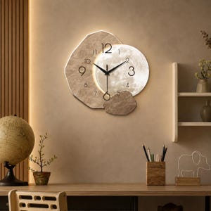 May include: A wall clock featuring an irregular, textured beige stone-like backing and a circular, illuminated moon-patterned face. The clock has black hour, minute, and second hands, with black numerals indicating the time against the light background.