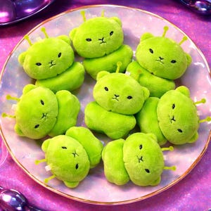 Pode incluir: Uma cole&ccedil;&atilde;o de brinquedos de pel&uacute;cia de ursos alien&iacute;genas verde lim&atilde;o com tra&ccedil;os faciais bordados em preto e antenas amarelas. Os brinquedos est&atilde;o dispostos em um prato iridescente rosa e branco, criando uma cena l&uacute;dica e divertida.
