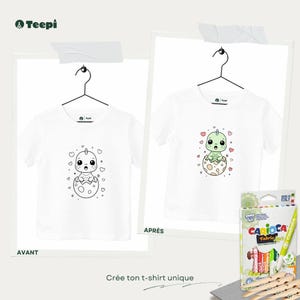 Peut inclure: Deux t-shirts blancs avec un motif de dinosaure, l'un en noir et blanc et l'autre en couleur, suspendus à des cintres. Une boîte de marqueurs pour tissu est également présente, avec le texte "Crée ton t-shirt unique".