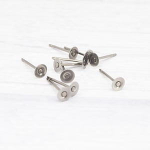 May include: A collection of silver-toned metal earring posts featuring a flat circular pad at the top for attaching decorative elements. These jewellery findings have a smooth, polished finish and a straight post extending from the centre of each disc.