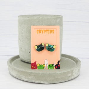 Aretes tipo rana Loveland: acrílico verde galaxia, postes de titanio