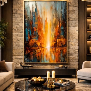 Peut inclure: Un tableau abstrait encadré d'or est le point central d'un salon. L'œuvre présente des coups de pinceau verticaux dans des tons d'orange, de bleu et de blanc, créant un effet de cascade. La pièce comprend une table basse ronde, un canapé et un mur en pierre.