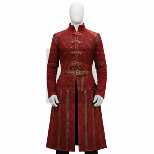 May include: A long, red coat with a high collar, three buckle closures, and a belt. The coat features decorative stitching, gold-colored studs, and vertical brown leather accents. The coat is displayed on a mannequin.