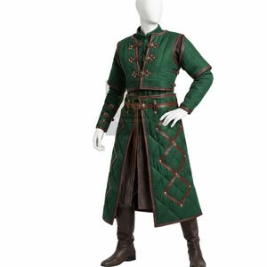 Puede incluir: Una chaqueta gambesón acolchada de color verde y un abrigo largo a juego con correas de cuero marrón, hebillas de metal y ribetes de cuero con patrón de diamantes. El conjunto incluye mangas largas con puños de hebilla y una falda interior marrón.