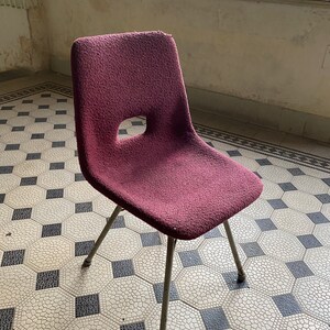 May include: A burgundy upholstered chair with a metal frame and four legs. The chair is sitting on a tiled floor with a geometric pattern.
