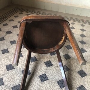 May include: A vintage wooden chair with a dark brown finish, viewed from underneath. The chair has a rounded seat and four legs. The legs are slightly angled, and the chair appears to be made of solid wood.