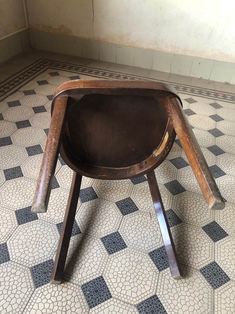 May include: A vintage wooden chair with a dark brown finish, viewed from underneath. The chair has a rounded seat and four legs. The legs are slightly angled, and the chair appears to be made of solid wood.
