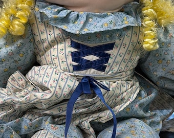 Cloth doll with blonde curly hair wearing blue floral dress and bonnet