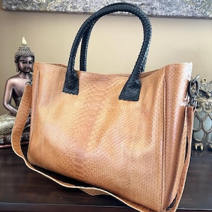 Può includere: Una borsa tote in pelle marrone con motivo a pelle di serpente. La borsa ha manici intrecciati neri e una tracolla staccabile. La borsa rettangolare offre un interno spazioso, ideale per l'uso quotidiano.