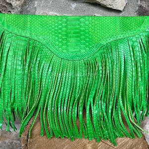Puede incluir: Bolso de mano verde brillante con flecos. El bolso está hecho de un material similar a la piel de serpiente y tiene un cierre de solapa. Los flecos largos cuelgan de la parte superior, agregando textura y movimiento al diseño.