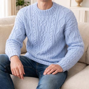 Peut inclure: Un pull bleu clair en tricot torsadé avec un col rond. Le pull présente des motifs torsadés complexes sur la poitrine et les manches. Le pull à manches longues est en matière douce et texturée.