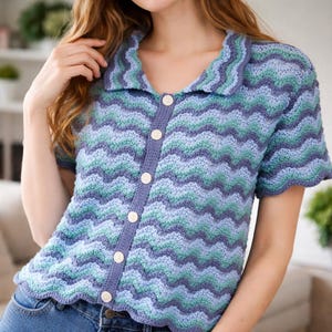 Peut inclure: Cardigan à manches courtes avec un motif ondulé bleu, vert d'eau et lavande. Le col et la patte de boutonnage sont de couleur lavande unie. Le cardigan a un bord festonné et est fait d'un fil doux et texturé.