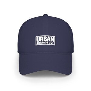 May include: A navy blue baseball cap with a curved peak. The cap displays the white text "URBAN THREADS CO." within a white rectangular border on the front. A classic style hat.