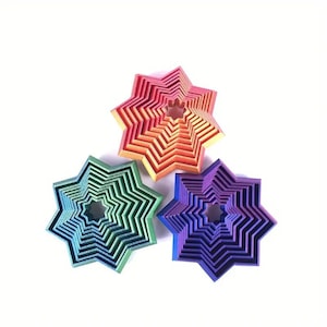 May include: Three star-shaped decorative objects in green, orange, and purple. Each star has a layered design, creating a three-dimensional effect. The objects are arranged on a white background.