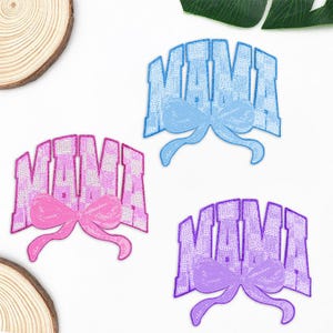 Peut inclure: Trois écussons brodés avec le mot "MAMA" dans une police universitaire, chacun avec un nœud. Un écusson est rose, un est bleu et un est violet. Les écussons sont sur un fond blanc.