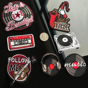 May include: A collection of embroidered patches with music-themed designs. Includes a record with "Love is Beautiful" text, a saxophone, a cassette tape, a turntable, and a record with headphones. The patches are in various colors, including red, black, and white.