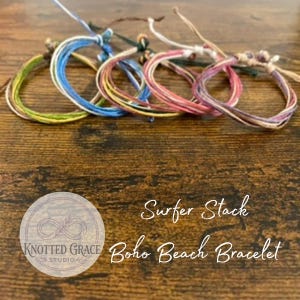 Puede incluir: Cinco pulseras de estilo surfero con detalles anudados se muestran sobre una superficie de madera. Las pulseras presentan varios colores, como azul, rosa, amarillo y verde. El texto "Surfer Stack Boho Beach Bracelet" es visible.