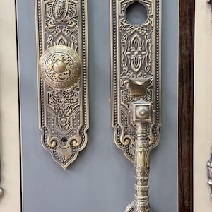 May include: A pair of antique brass door hardware pieces featuring intricate embossed scrollwork and floral patterns. The left piece includes a round knob, while the right piece features a vertical handle with a thumb latch mechanism and a keyhole.