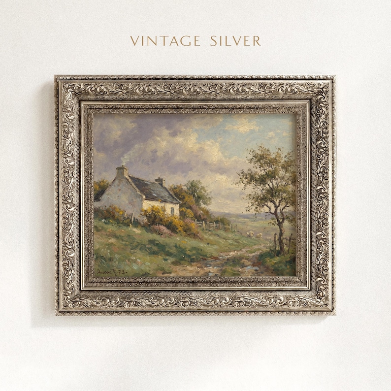Vintage oil painting of a white stone cottage with a gray roof on a green hillside, surrounded by flowering bushes, a lone tree, and a dirt path under a cloudy sky, displayed in an ornate gold frame.