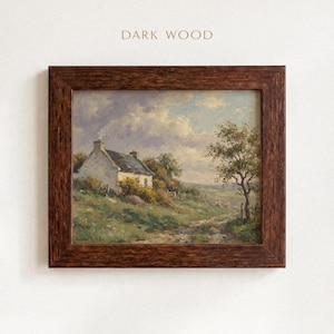 Vintage oil painting of a white stone cottage with a gray roof on a green hillside, surrounded by flowering bushes, a lone tree, and a dirt path under a cloudy sky, displayed in an ornate gold frame.