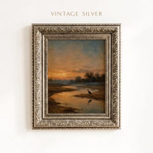 May include: A landscape painting in a decorative silver frame with ornate scrollwork. The artwork depicts a river winding through a marsh at sunset with a heron standing on the bank. The text VINTAGE SILVER is printed above the frame.