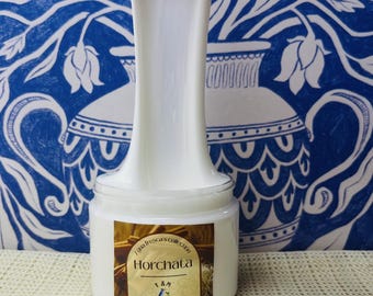 May include: A clear plastic jar filled with white, viscous slime. A portion of the slime is being pulled upward in a long, smooth strand. The jar features a label with the text "Agua fresca's collection", "Horchata", "T & M", and "SLIMES".