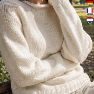 May include: A long-sleeved, off-white knitted sweater featuring a round neckline and ribbed cuffs at the wrists and hem. The garment is crafted from a soft, textured yarn with a consistent knit pattern throughout the body and sleeves.