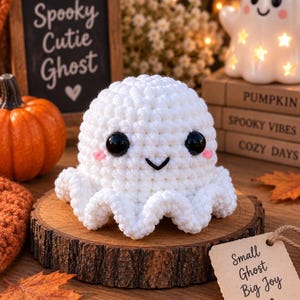 May include: A white crocheted ghost plush toy with large black plastic eyes, a stitched black mouth, and small pink embroidered cheeks. The ghost has a rounded head and a ruffled, wavy base, crafted with a textured yarn finish.