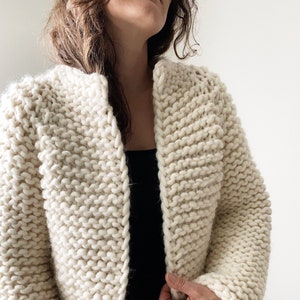 K&ouml;nnte beinhalten: Ein cremefarbener Strickcardigan mit leicht verk&uuml;rzter L&auml;nge und einem einfachen offenen Vorderteil.