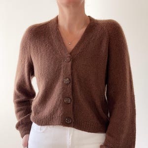 以下が含まれることがあります： Vネックとボタン留めで、茶色のふわふわしたカーディガン。長袖で、丈が短めです。