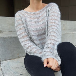 Könnte beinhalten: Ein grauer und weiß gestreifter Strickpullover mit lockerer Passform und langen Ärmeln.