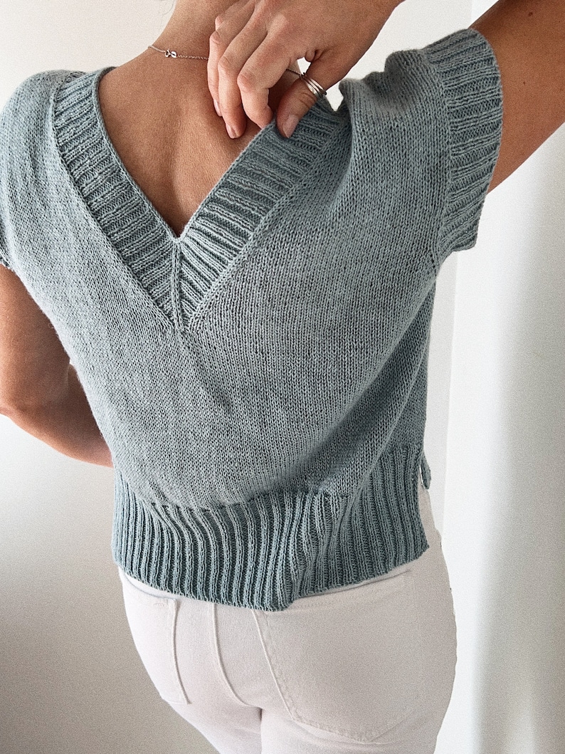 May include: A light blue knitted top with a V-neck and short sleeves.