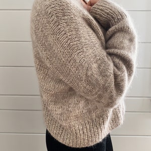 May include: A soft, beige knitted sweater with a V-neck and long sleeves.