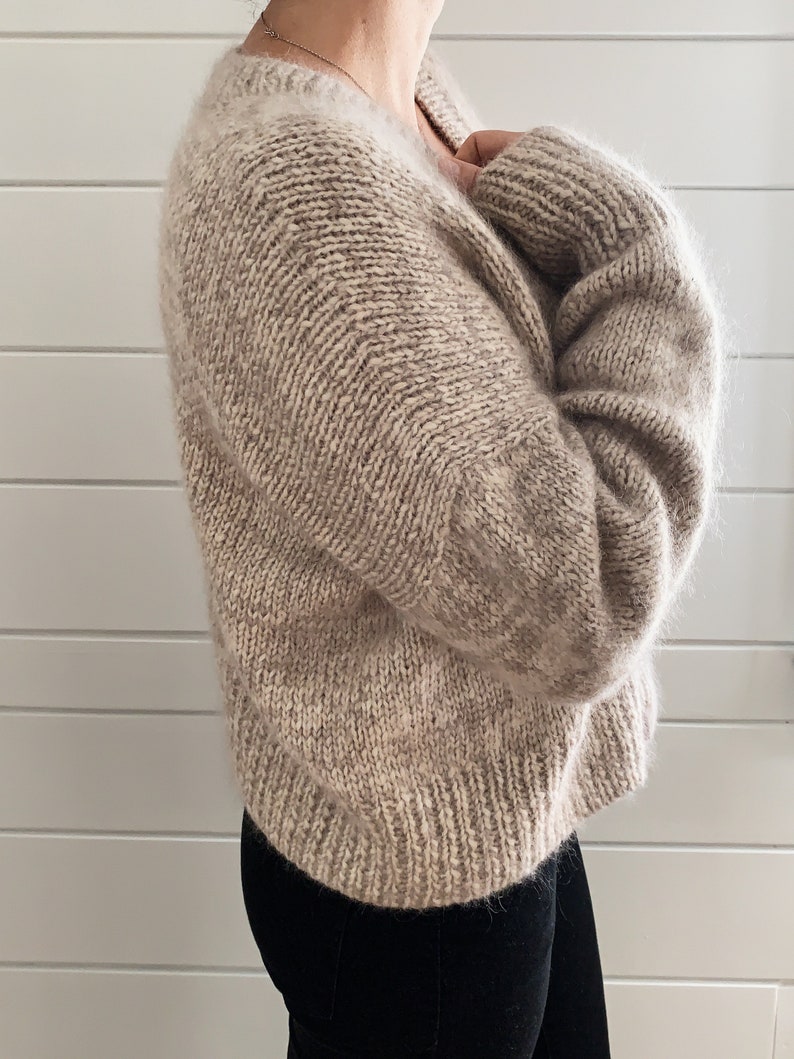 May include: A soft, beige knitted sweater with a V-neck and long sleeves.