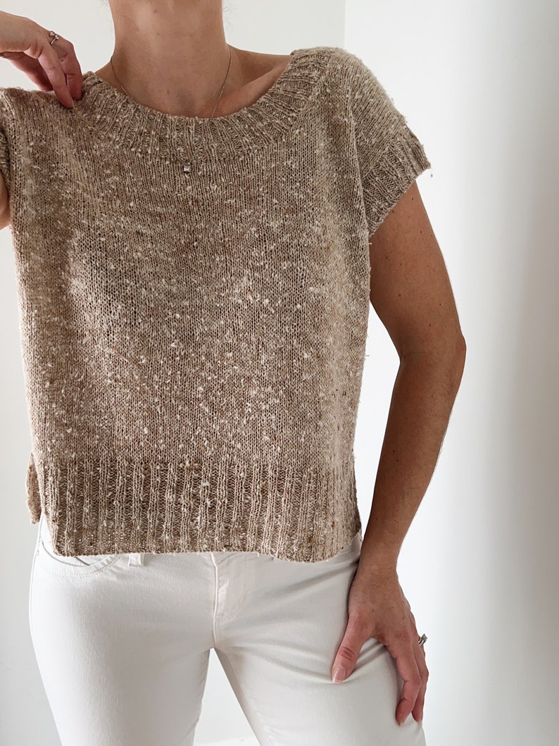 May include: A beige knitted top with short sleeves. The top has a speckled texture and a round neckline.