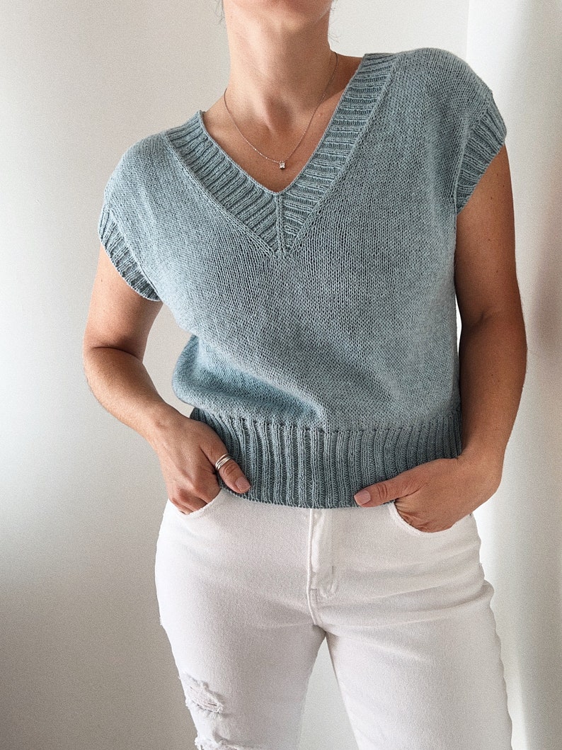 May include: A light blue sleeveless knitted sweater with a v-neck and a ribbed hem.