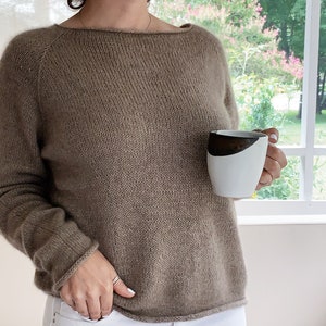 May include: A brown knitted jumper with a boat neck and long sleeves. The jumper is made of a soft, comfortable material and has a relaxed fit.