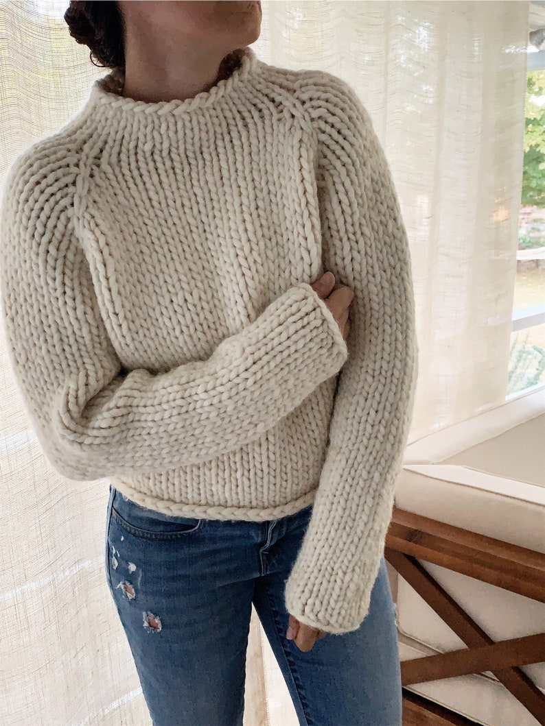 May include: A cream-colored chunky knit sweater with a high neckline and long sleeves.