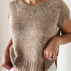 May include: A beige knitted top with short sleeves and a round neckline. The top has a speckled texture.